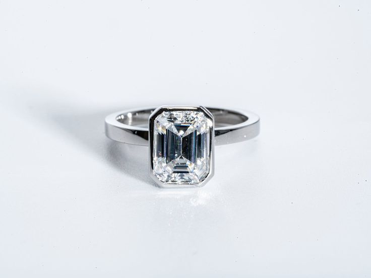 an emerald - cut diamond ring on a white surface, with the center stone visible