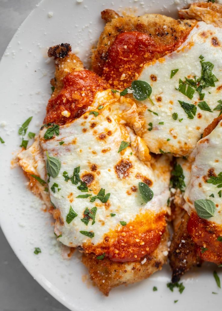 a white plate topped with lasagna covered in sauce and parmesan cheese