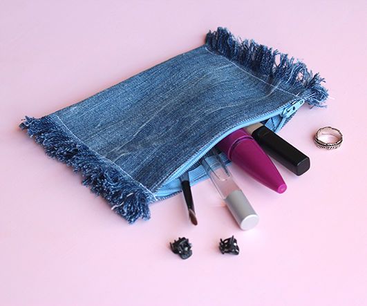 the contents of a denim purse are laid out on a pink surface, including lipstick, mascara, and other items