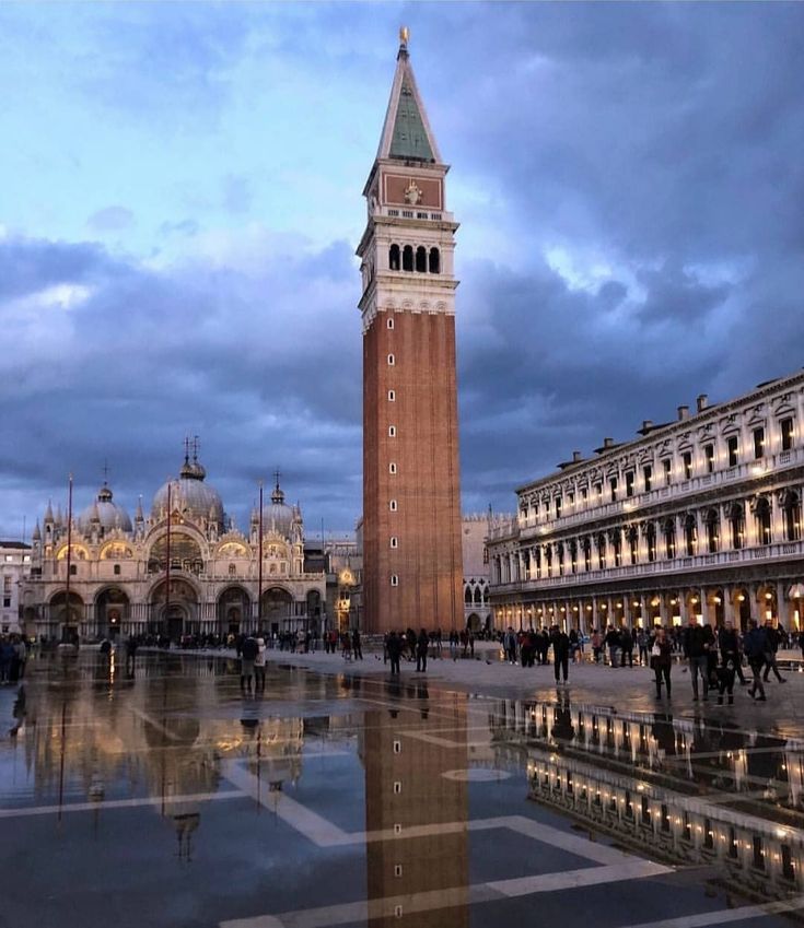 a tall clock tower towering over a city filled with buildings and people walking around it