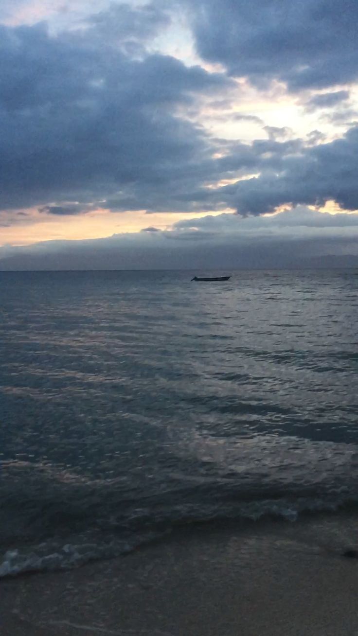 a boat is out on the water at sunset or sunrise in the distance, with dark clouds above it