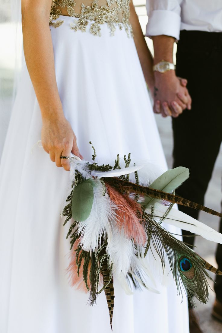 a bride and groom holding hands with feathers