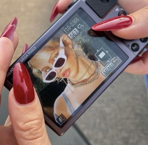 a woman with red nail polish holding up her cell phone to take a picture on the screen