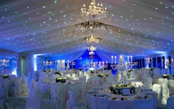 a banquet hall with white linens, chandeliers and blue uplighting