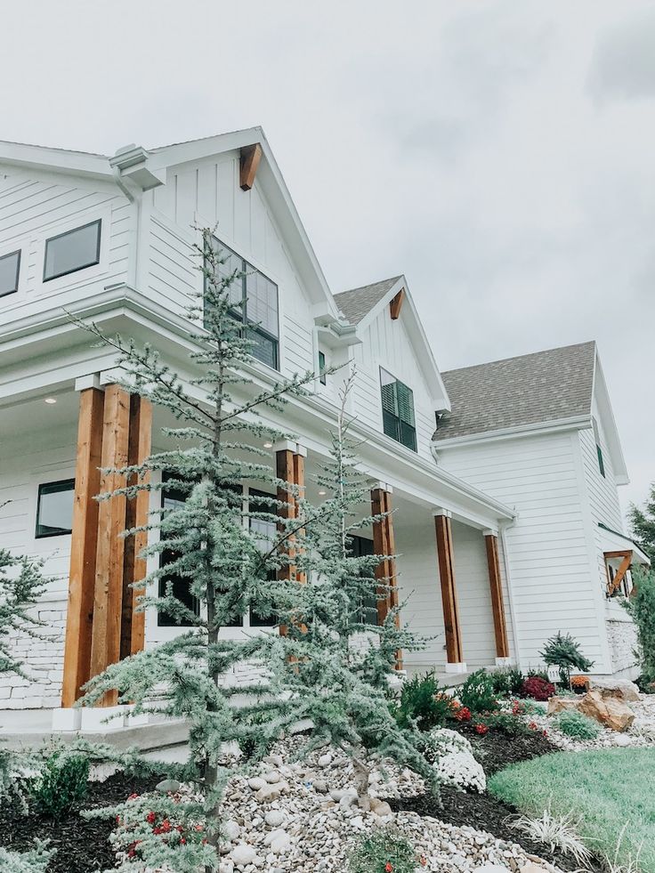 a white house with snow on the ground and evergreen trees in front of it,