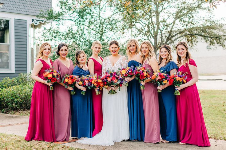 a group of women standing next to each other in front of a house holding bouquets