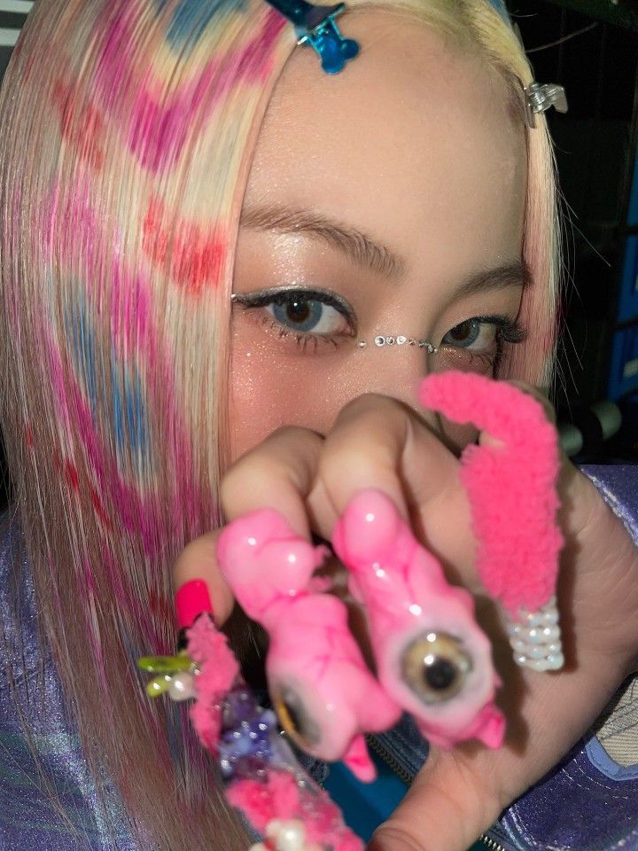 a girl with pink and blue hair is holding up some small toys in her hands