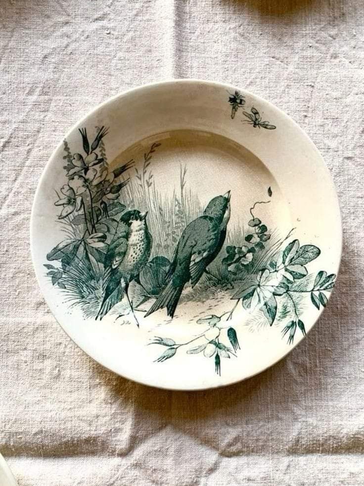 a plate with birds painted on it sitting on a white table cloth next to other plates