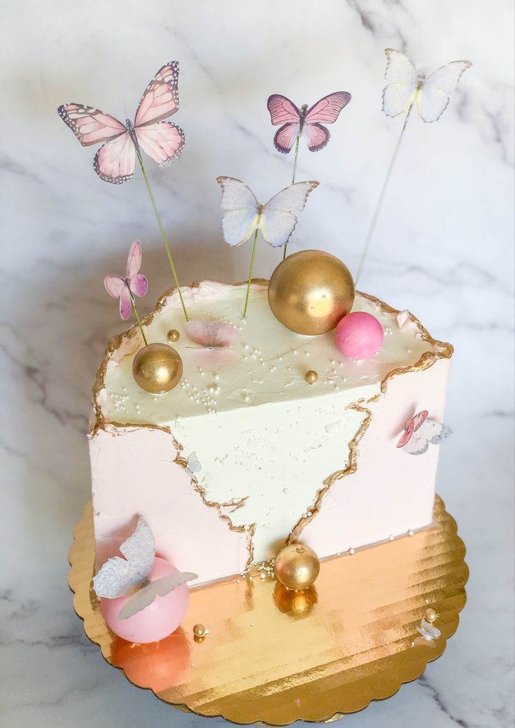 a cake decorated with gold, pink and white butterflies on top of a marble table