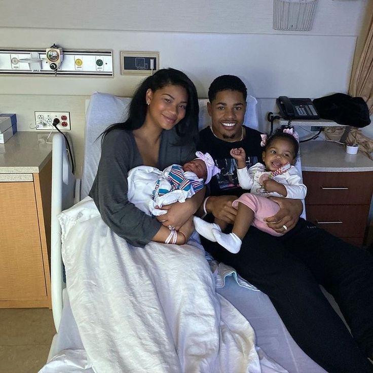 a man and woman are sitting in a hospital bed with their two babys, smiling at the camera