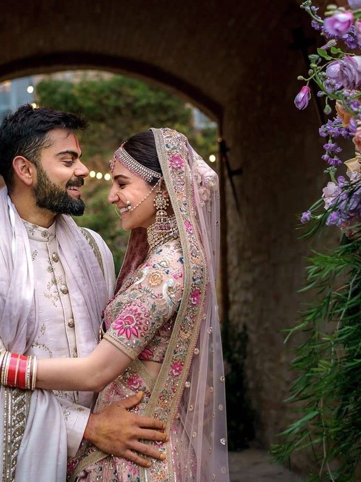 a man and woman standing next to each other in front of a flower covered archway