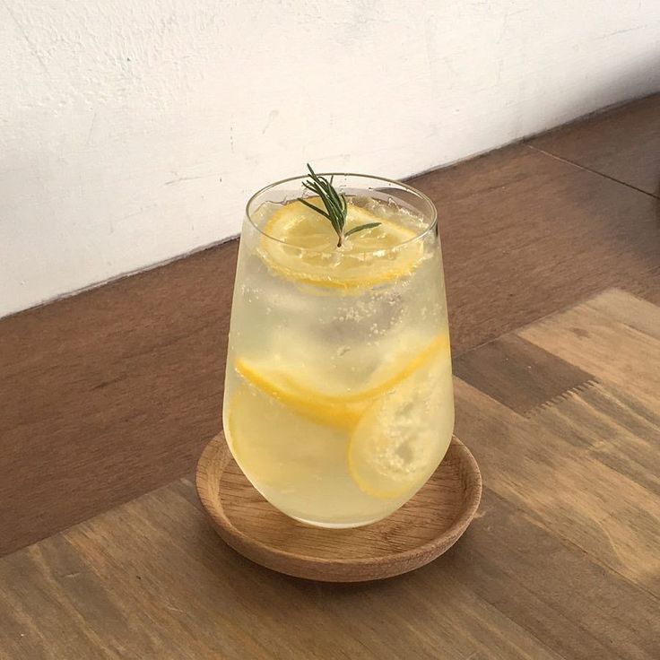 a glass filled with lemon and rosemary on top of a wooden plate next to a wall