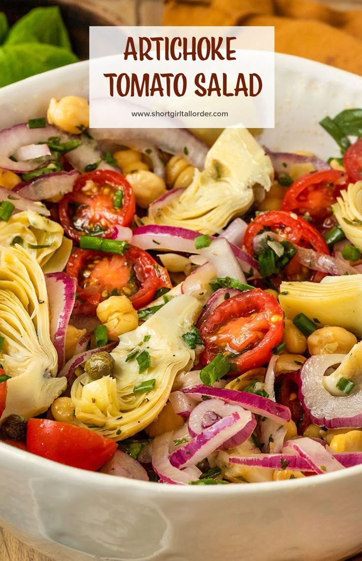 artichoke tomato salad in a white bowl with red onions, corn and tomatoes