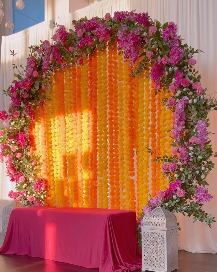 an orange and pink backdrop with flowers on the wall next to a white table cloth