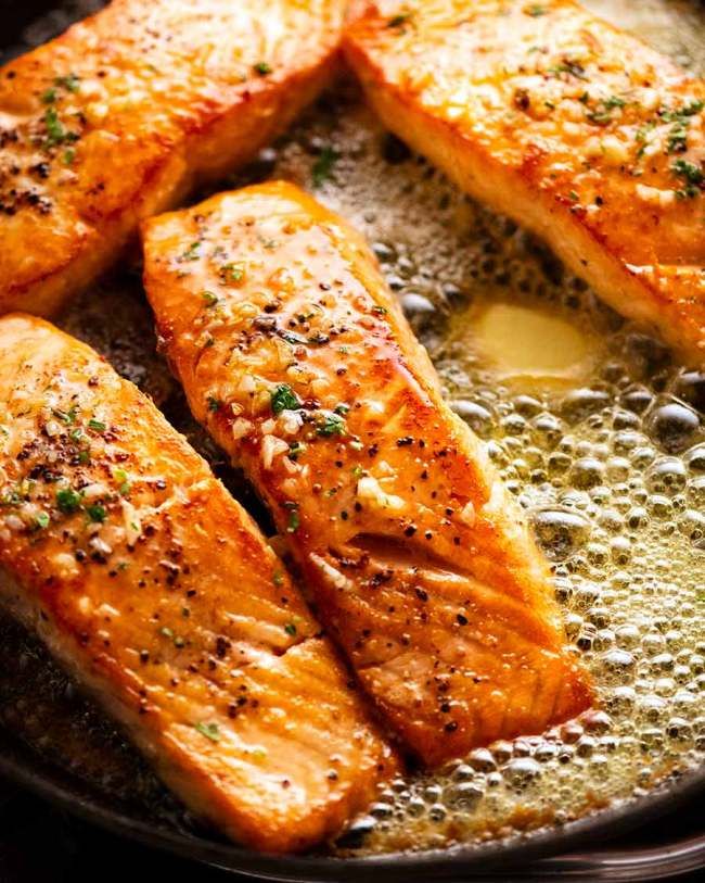 salmon cooking in a skillet with oil and seasoning on the side, ready to be cooked