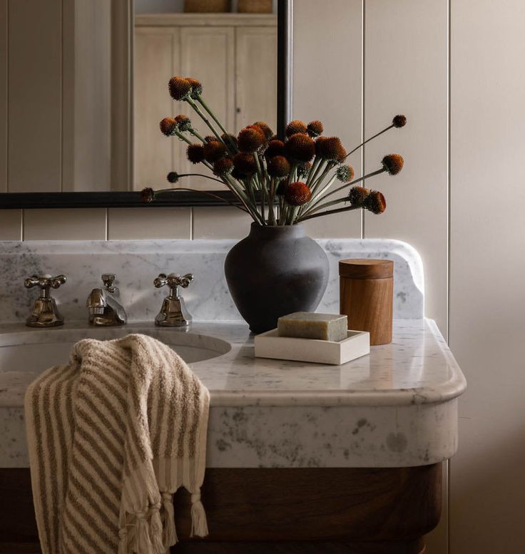 a bathroom sink with flowers in a vase on top of it and a towel next to it