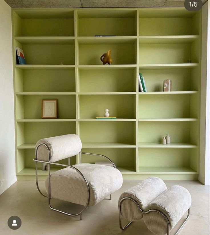 a living room with green bookshelves and two chairs in front of the bookcase