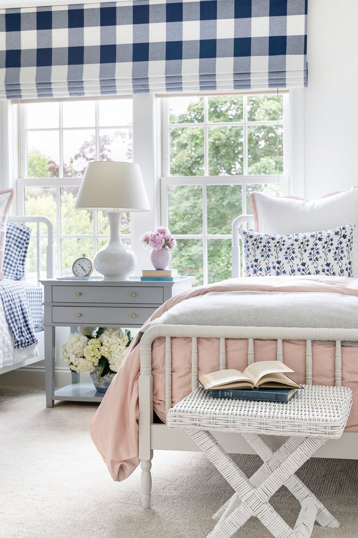 a bedroom with blue and white checkered curtains, pink bedding, and a book on the end table