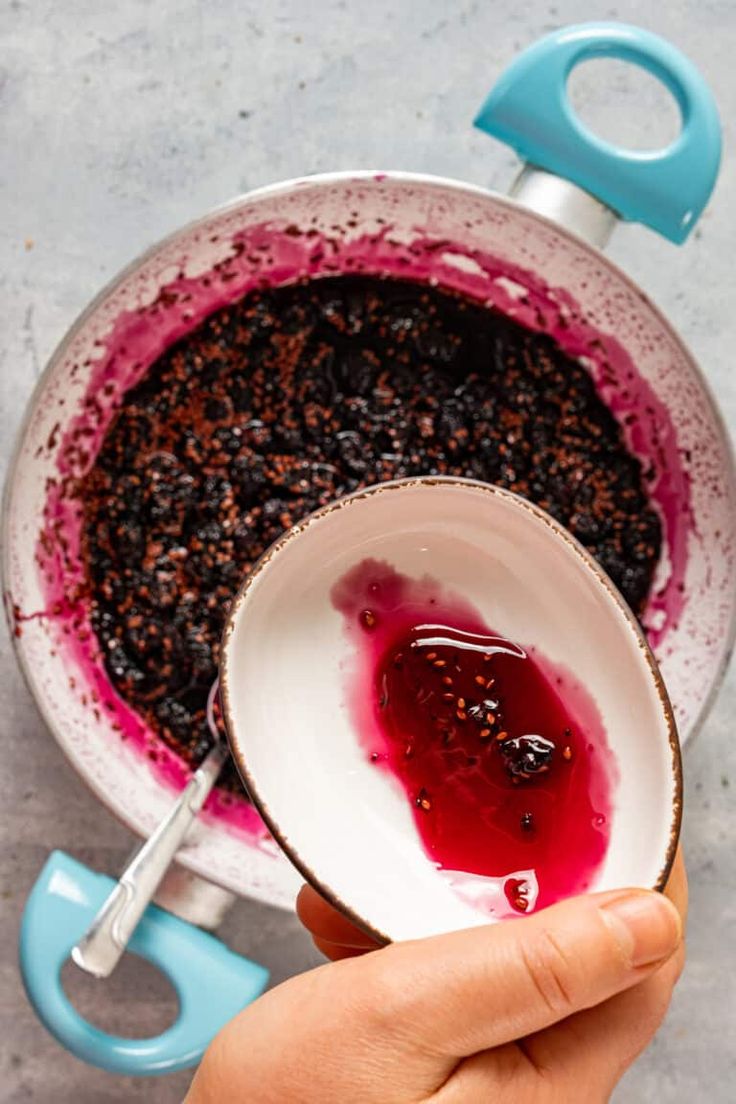 a person holding a spoon in a bowl filled with berries and other things to eat