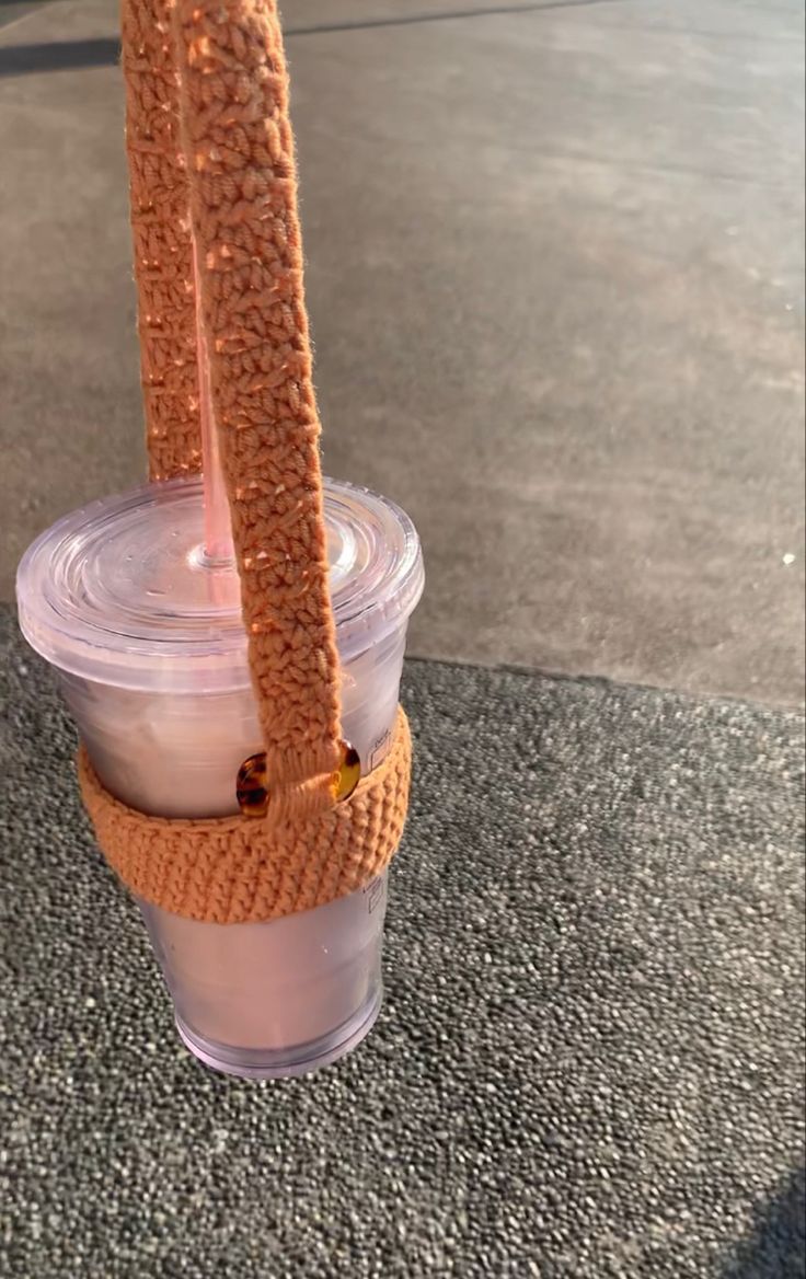 a cup that is sitting on the ground with a knitted handle attached to it