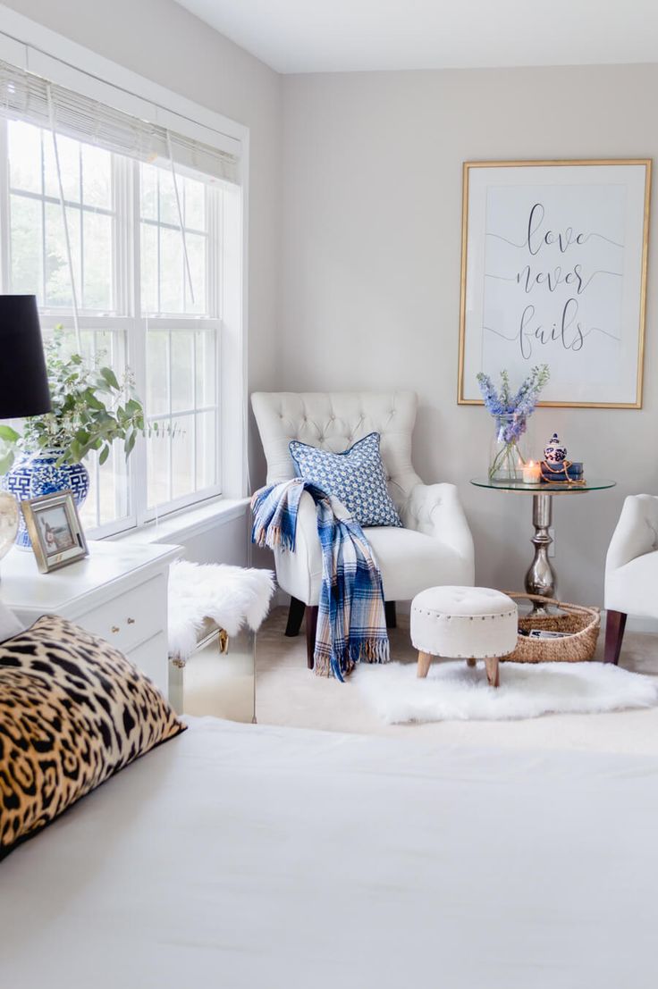 a bedroom with two white chairs and a leopard print pillow on the bed in front of a window