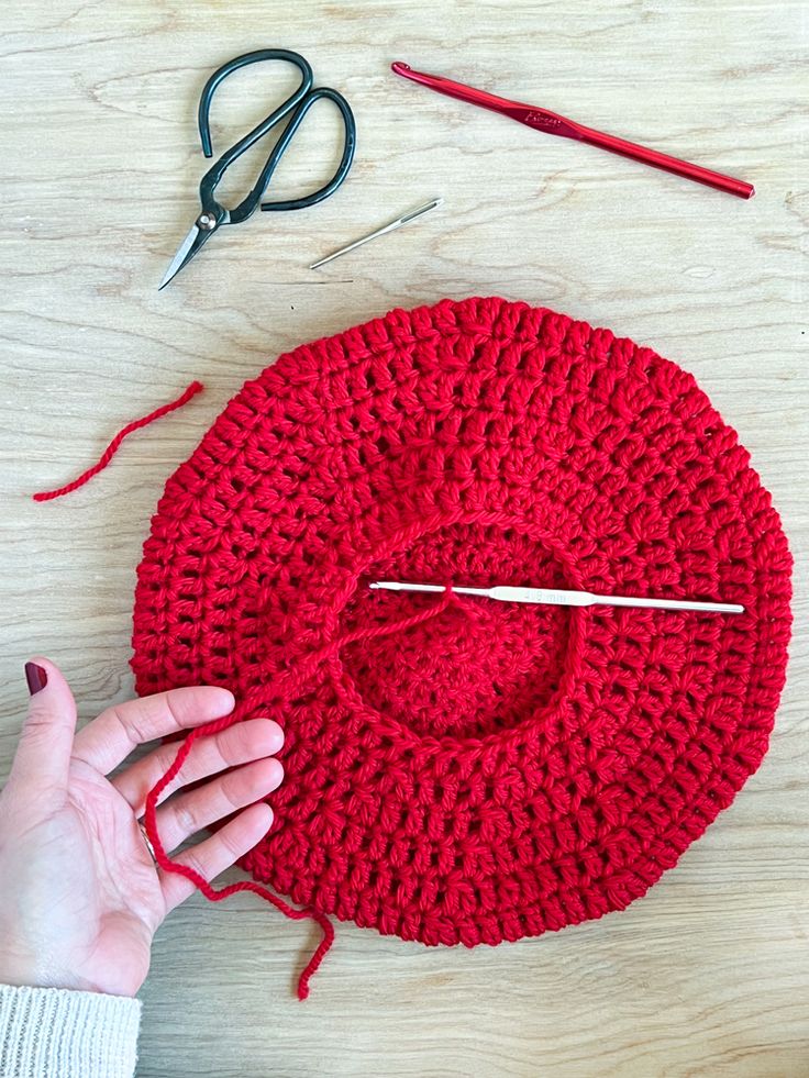 someone is crocheting a red hat with scissors and yarn