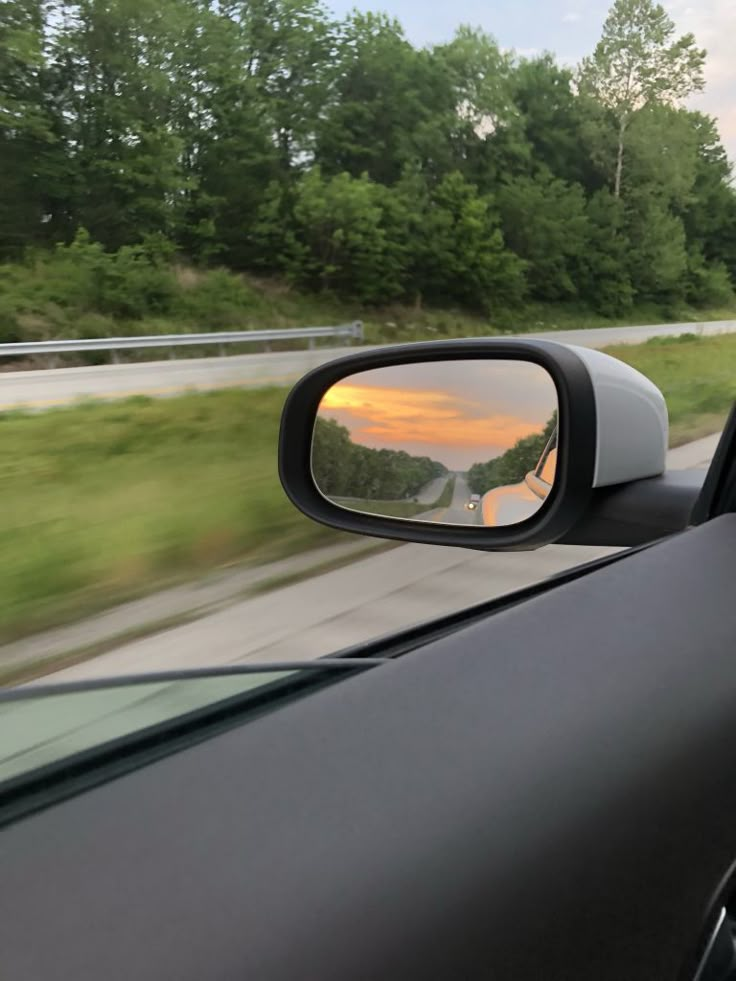 the rear view mirror of a car is reflecting trees and road in it's reflection