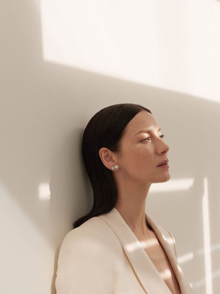 a woman leaning against a white wall with her head turned to the side and eyes closed