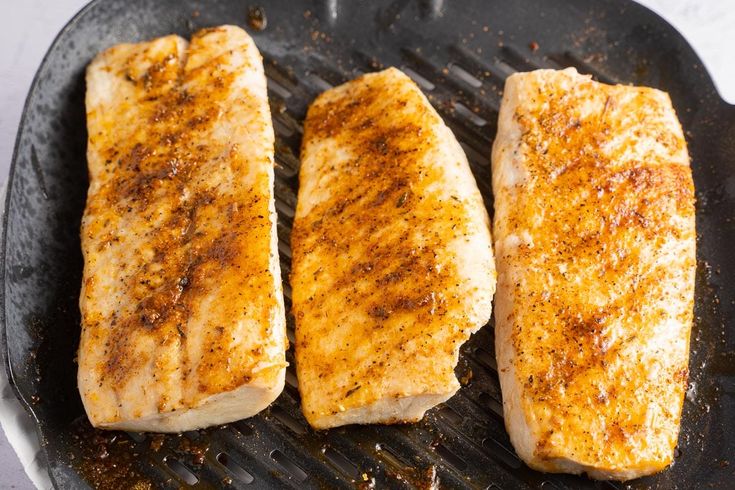 three pieces of fish are cooking on a grill