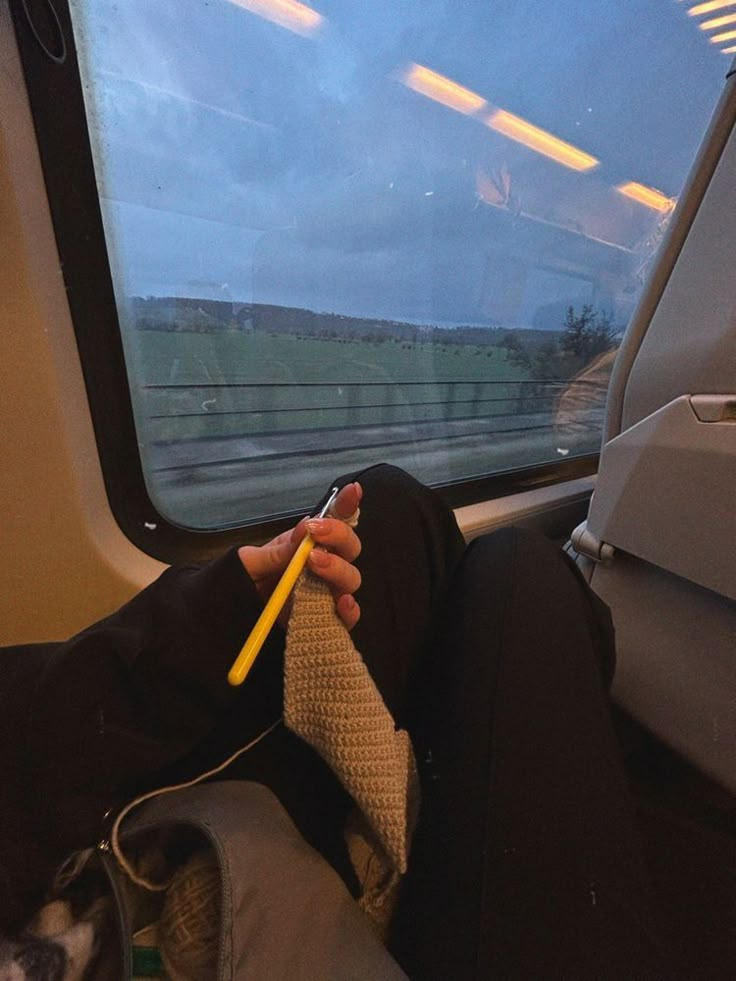 a person sitting on a train holding a yellow pencil in their hand and looking out the window