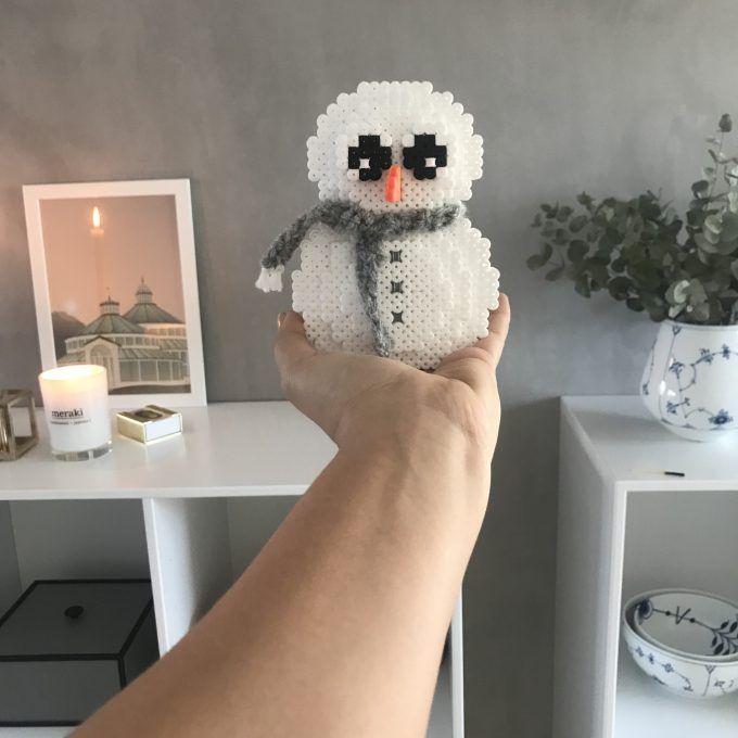 a person holding up a small white snowman ornament in front of a table