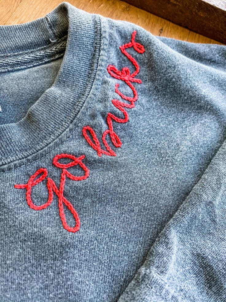 a gray shirt with red writing on it sitting on top of a wooden floor next to a window