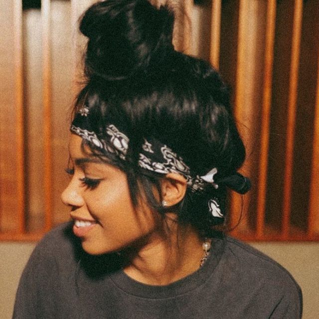 a woman wearing a bandana and looking at her cell phone while sitting in front of a wood paneled wall