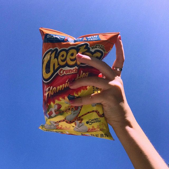 a hand holding a bag of cheetos against a blue sky