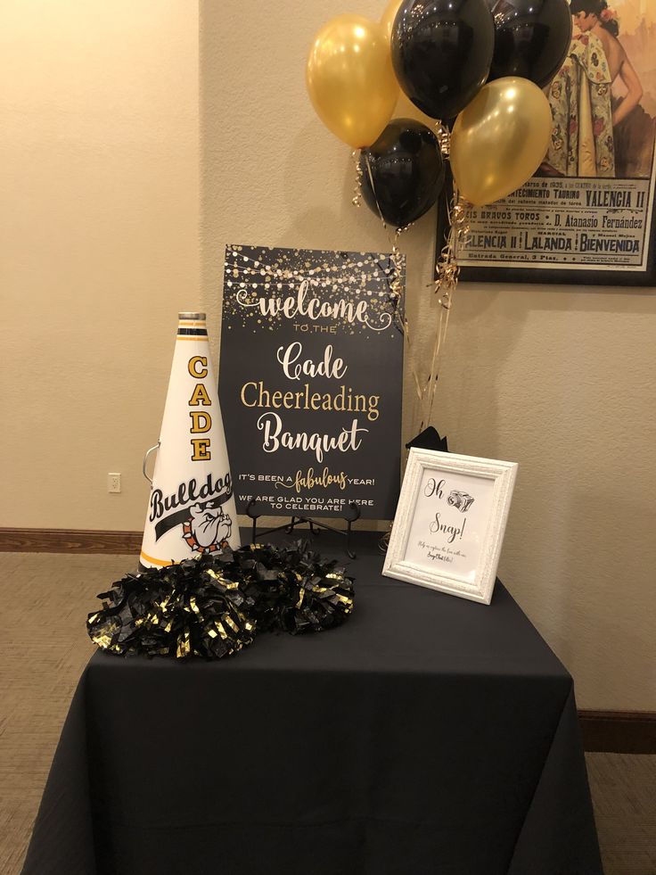 a black table topped with balloons next to a sign and some confetti cones