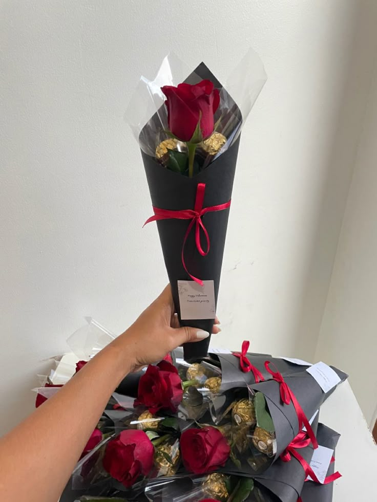 a person holding a bouquet of roses on top of a pile of chocolates and wrapped in cellophane