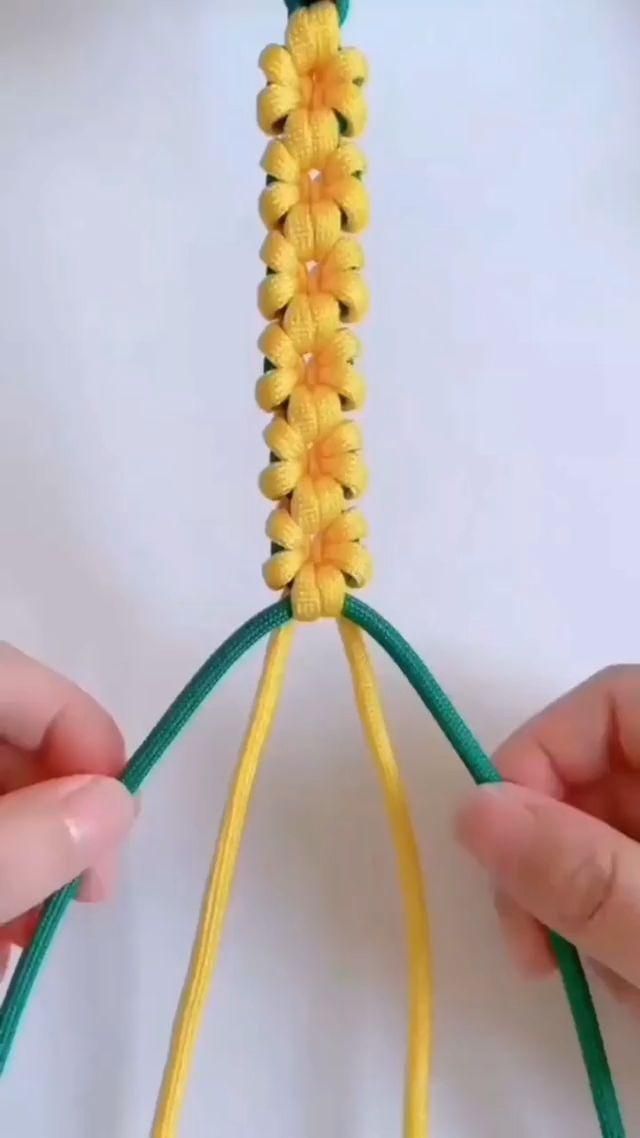 two hands are working on a piece of yellow and green yarn