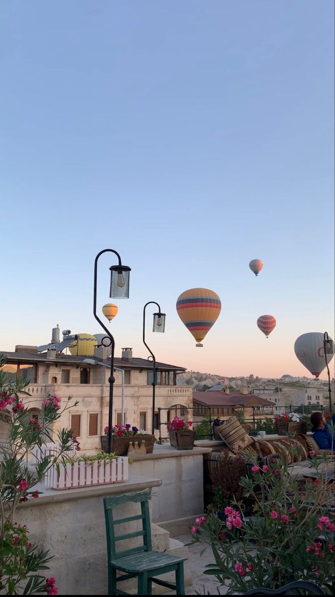 several hot air balloons are flying in the sky above some buildings and flowers on a balcony