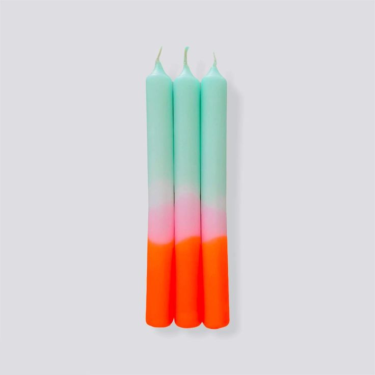 two orange and green candles sitting next to each other on a white surface with one candle in the middle