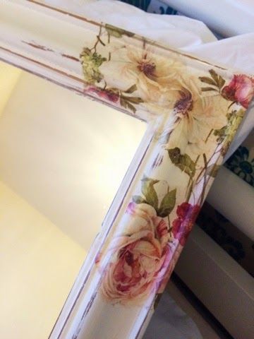 a mirror with flowers painted on it sitting next to a white box and some candles