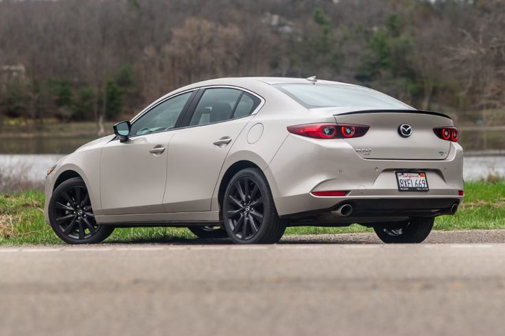 a white mazda car parked on the side of the road next to some grass and trees