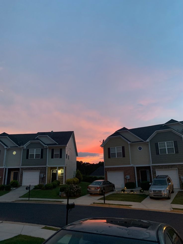 two houses with cars parked on the street in front of them at sunset or dawn