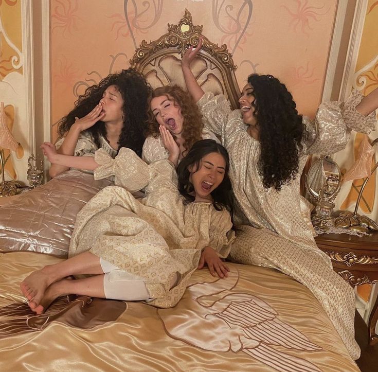 four women are laying on a bed and posing for the camera with their arms in the air