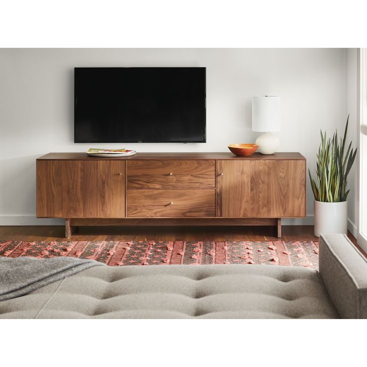 a flat screen tv sitting on top of a wooden cabinet in a living room next to a window