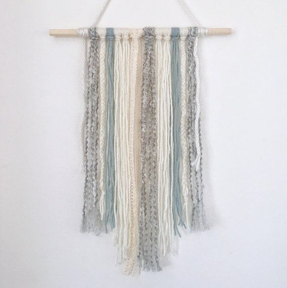 a white wall hanging with multicolored tassels and wooden pegs on it