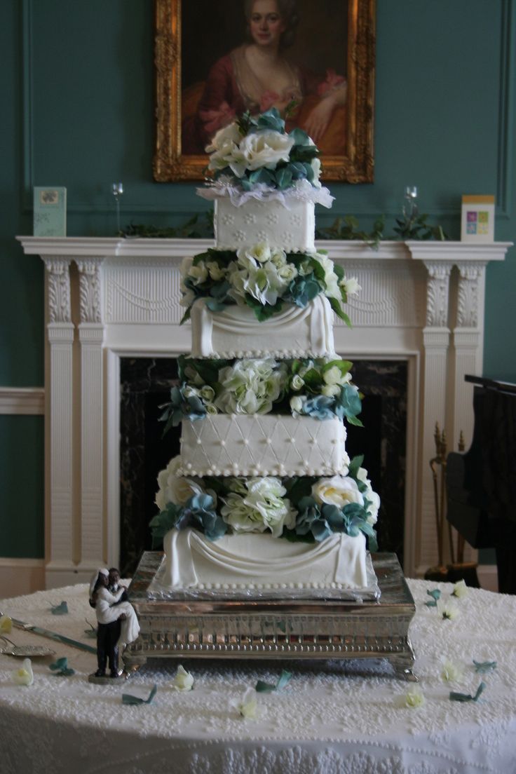 a four tiered wedding cake sitting on top of a table in front of a painting