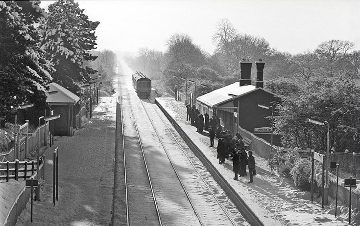 black and white photograph of people walking on the side of train tracks near a station