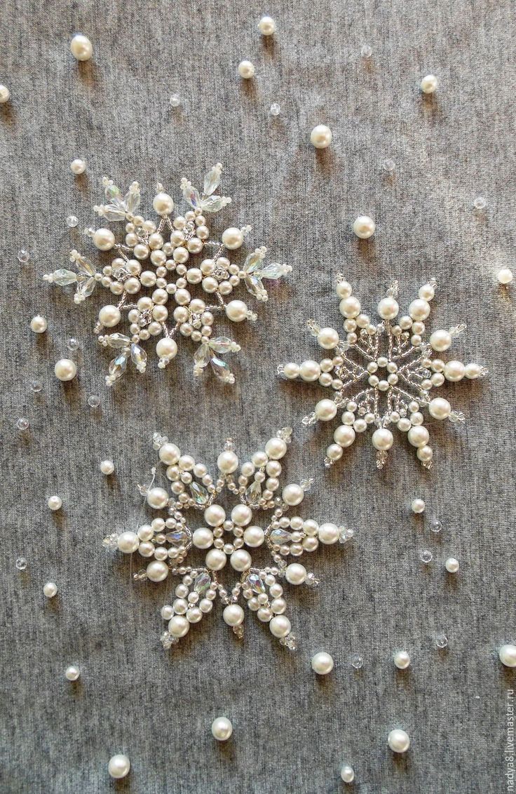 three snowflakes with pearls and beads on a gray cloth covered in white thread