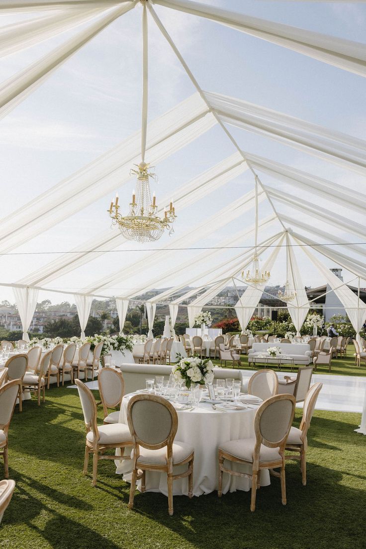 tables and chairs are set up under a tent for an outdoor wedding reception with chandeliers