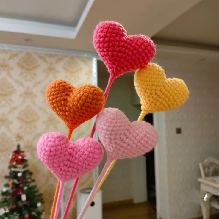 four crocheted hearts are on sticks in front of a christmas tree and wall